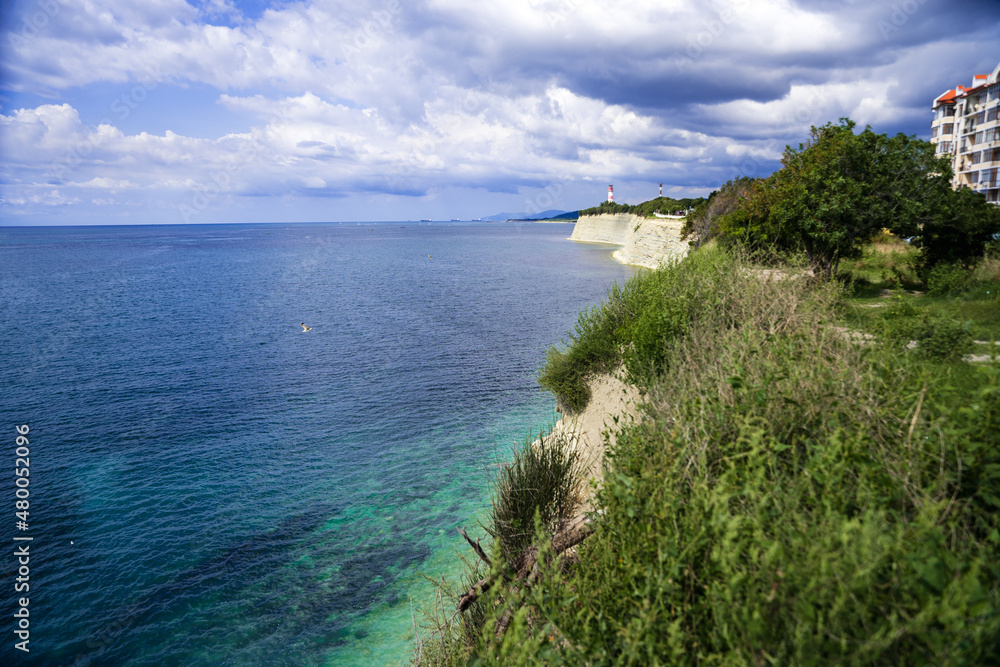 High rocky coast of the Black Sea. High layered rocks. Lighthouse on the seashore. Blue sea summer, white clouds.