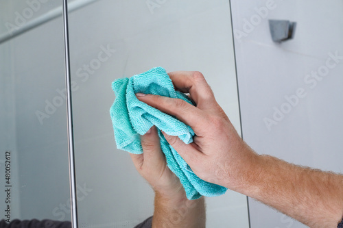A man wipes a mirror cabinet in the bathroom with a rag. Cleaning of the house, bathroom.