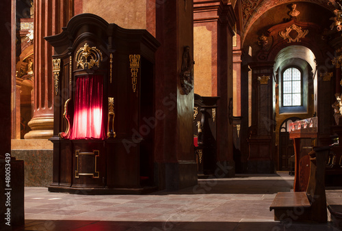 Confessional lit up in red, priest inside, baroque interior of the parish church, Poznan, Poland, photo