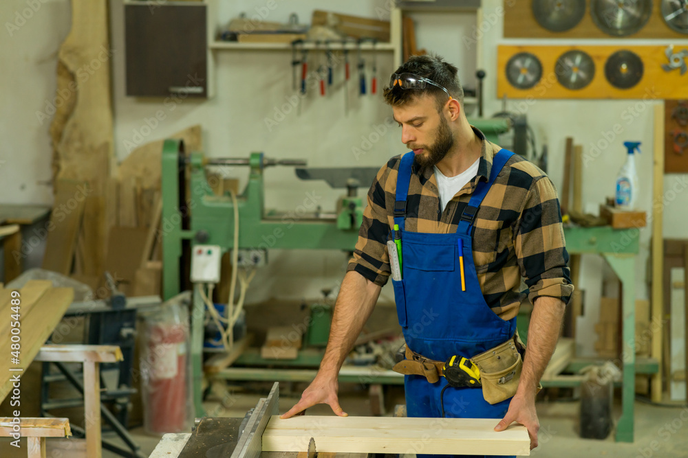 Handsome carpenter preparing, measures and cutting boards on cutting machine Handsome carpenter preparing, measures and cutting boards on cutting machine