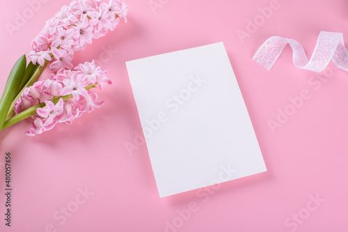 Blank wedding invitation stationery card mockup on pink background with hyacinth flowers and white ribbon, feminine blog flat lay, top view. Minimalist mockup 5x7 ratio, similar to A6, A5