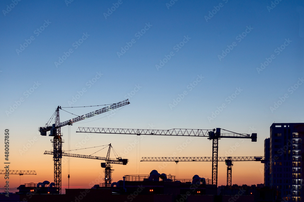 Silhouettes of tower cranes on construction site at sunset