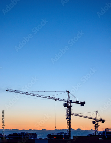 Silhouettes of tower cranes on construction site at sunset