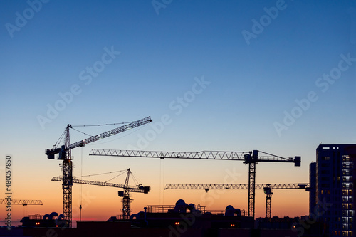 Silhouettes of tower cranes on construction site at sunset