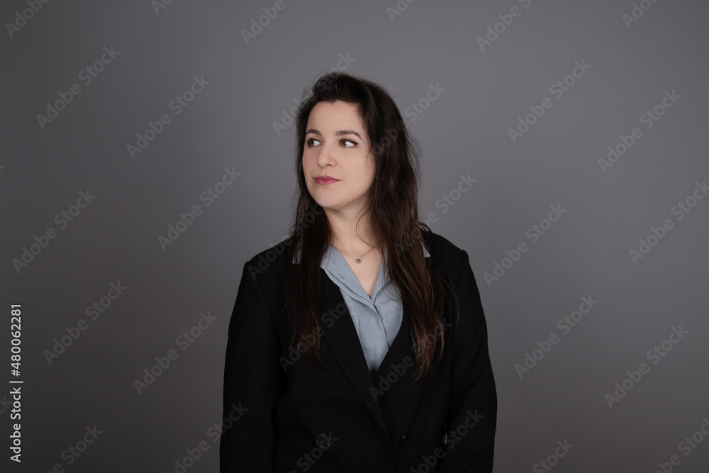 attractive confident brunette business woman in blue blouse and black jacket on grey background. attractive confident brunette business woman in blue blouse and black jacket on grey background.