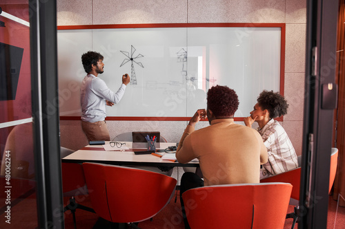 Young man discussing something on white board with his colleagues during a meeting