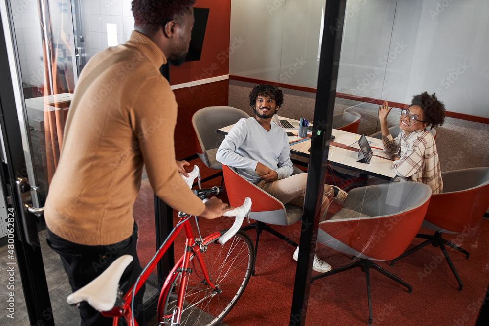 Fototapeta premium Stylish multiracial man entering with bike walking inside the coworking room