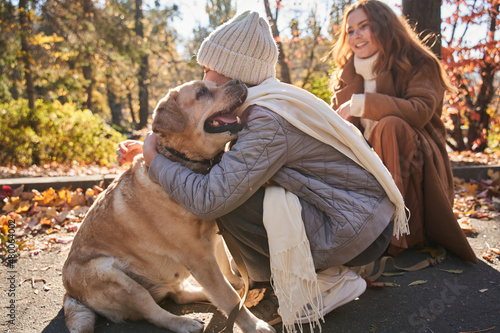Teenage girl embracing her lovely dog while sitting at the autumn forest with her mother
