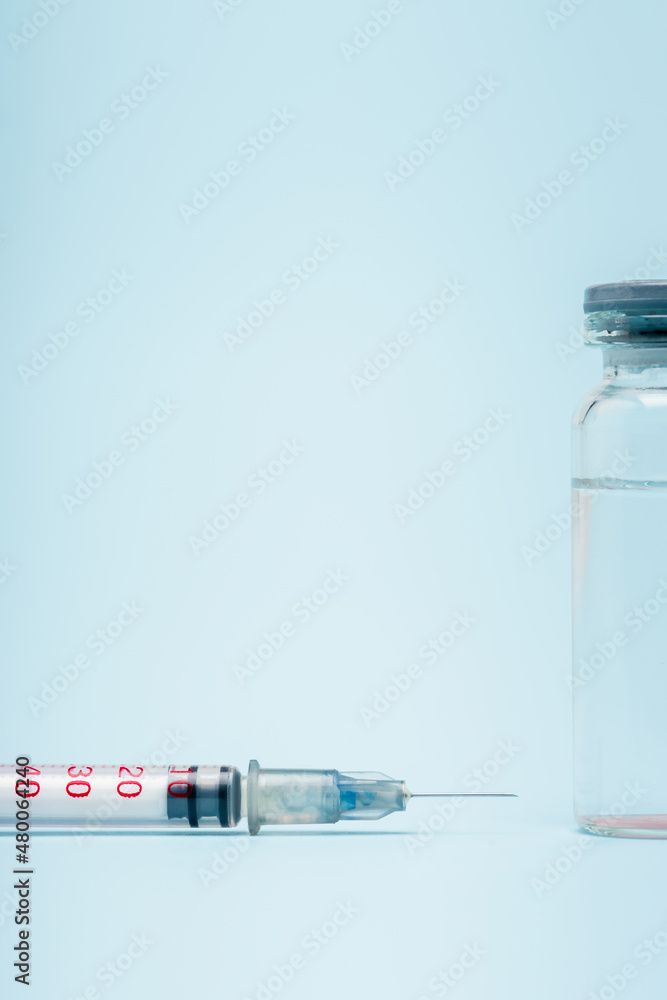 close up view of vaccine bottle near syringe on blue background, omicron variant concept. close up view of vaccine bottle near syringe on blue background, omicron variant concept.