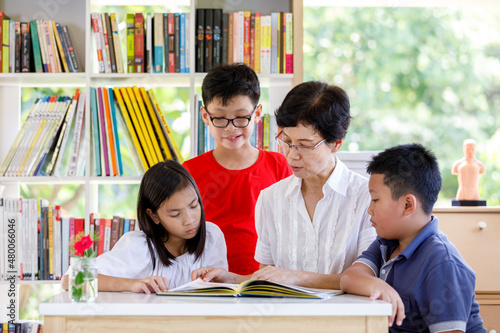 A Group of Asian Student Kid Reading a book with women teacher in School library with Shelf of Books in Background, Asian Kid Education Concept