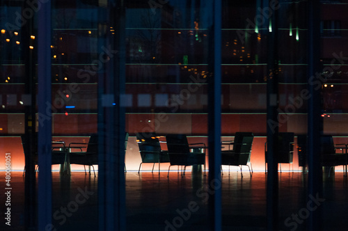 Blick durch Glasfassade in verlassene beleuchtete Lobby mit Bürostühlen