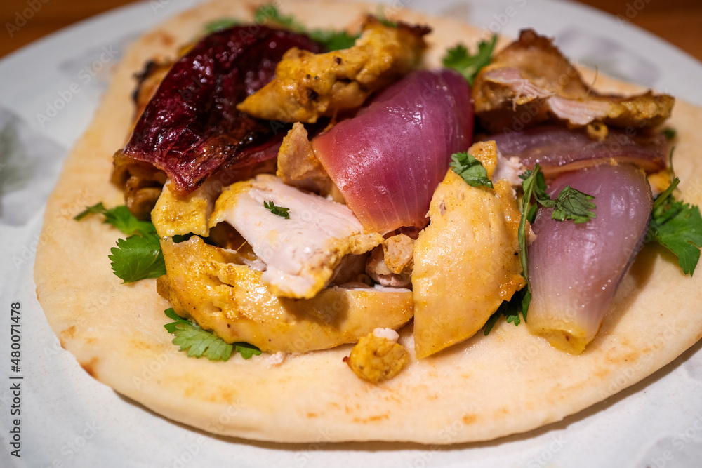 Chicken Souvlaki in a pita with onion, cilantro, and yogurt sauce. Delicious Greek dish served in the open pita on a white plate. Chicken Souvlaki in a pita with onion, cilantro, and yogurt sauce. Delicious Greek dish served in the open pita on a white plate.