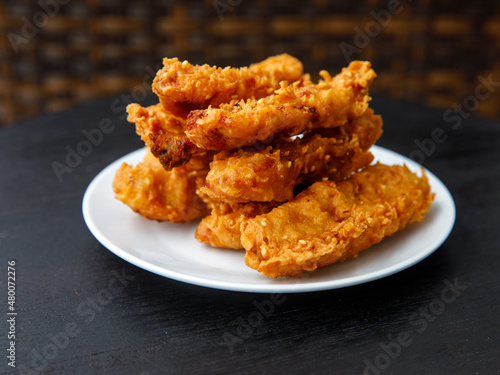deep-fried fritters sliced banana, also known as Kluay khek, served on white plate on black wooden table.