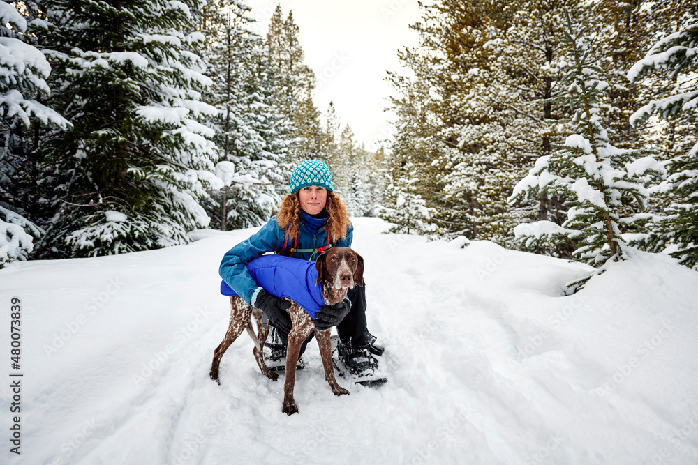 a young woman and her dog snowshoeing on a mountain trail Stock Photo