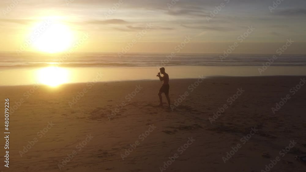 A drone shot with lots of dynamic movements, following a man practicing Muay Thai on a beach, with the sunset as a background. A drone shot with lots of dynamic movements, following a man practicing Muay Thai on a beach, with the sunset as a background.