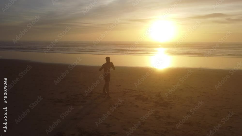 A low orbit drone shot of a man practicing Muay Thai on a beach, with the sunset as a background. A low orbit drone shot of a man practicing Muay Thai on a beach, with the sunset as a background.