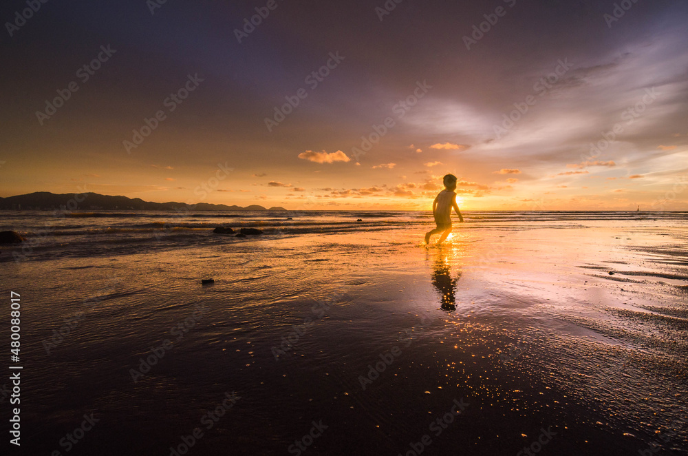 Beautiful sunset scenery at the beach with a silhouette of a young boy playing and running