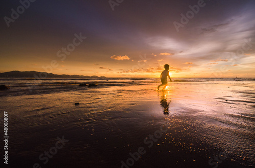 Beautiful sunset scenery at the beach with a silhouette of a young boy playing and running