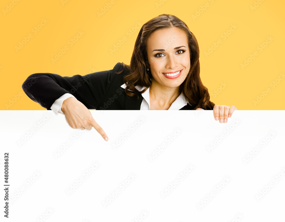 Cheerfully smiling brunette business woman in blue clothing, standing behind, peeping from blank banner or mock up signboard, showing copy space for text, over orange yellow background. Cheerfully smiling brunette business woman in blue clothing, standing behind, peeping from blank banner or mock up signboard, showing copy space for text, over orange yellow background.