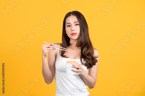 Sexy beautiful woman. She holds a cup of instant noodles on a yellow background.