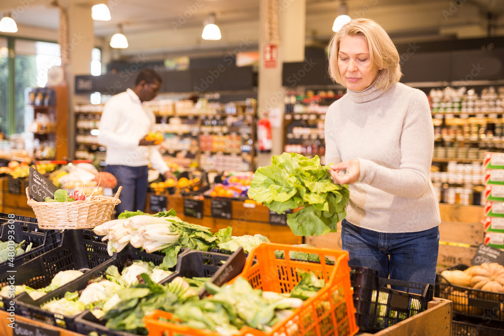 Portrait of pensive mature woman buying fresh organic vegetables in supermarket