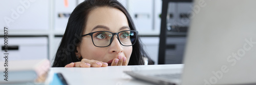 Bilde på lerret Shocked young woman looks from under table at laptop monitor closeup