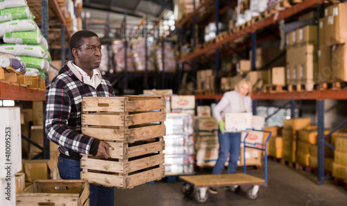 Focused African American warehouse worker stacking empty wooden boxes ..