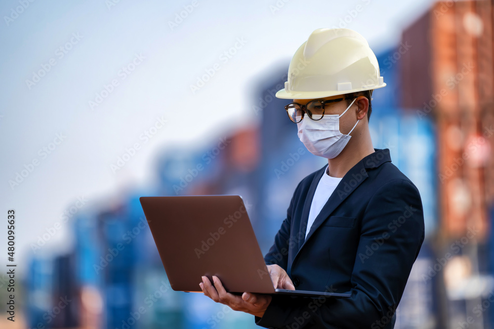 An Asian businessman in a black suit holds a laptop to inspect a container yard. An Asian businessman in a black suit holds a laptop to inspect a container yard.