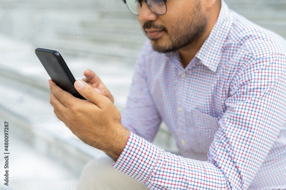 Bearded businessman smiling wearing glasses showing modern smartphone device typing text message in social media while sitting on stairs outdoor. Happy male spending free time in break of working. Bearded businessman smiling wearing glasses showing modern smartphone device typing text message in social media while sitting on stairs outdoor. Happy male spending free time in break of working.