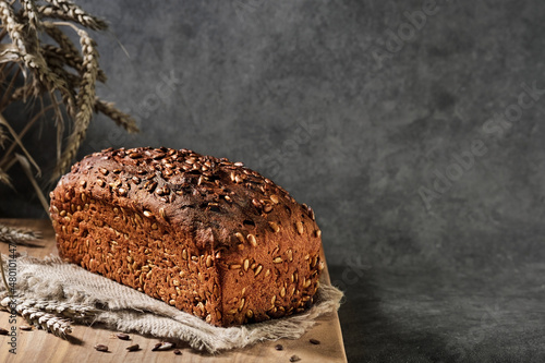 Homebaked bread. Healthy wheat and rye bread with seeds on sacking, close-up with selective focus. Naturally fermented bread, healthy food. Loaf on gray background with space for text