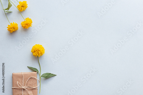 Gift box and yellow flowers on a light background, top view. The concept of congratulations.