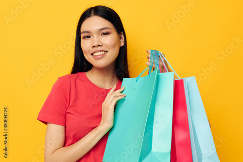 Portrait Asian beautiful young woman with multicolored shopping bags yellow background unaltered