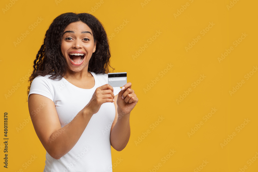 Overjoyed african american lady holding credit card in hand, posing over yellow studio background with copy space Overjoyed african american lady holding credit card in hand, posing over yellow studio background with copy space