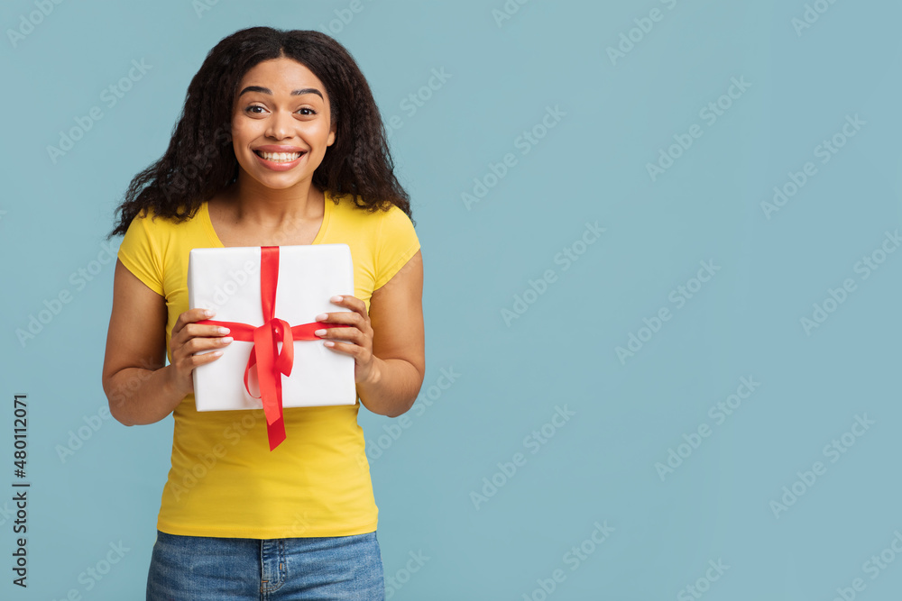Overjoyed young black lady holding gift box over blue studio background, panorama with free space Overjoyed young black lady holding gift box over blue studio background, panorama with free space