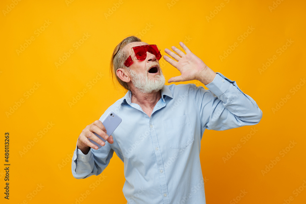 Senior grey-haired man in fashionable red glasses with a phone isolated background