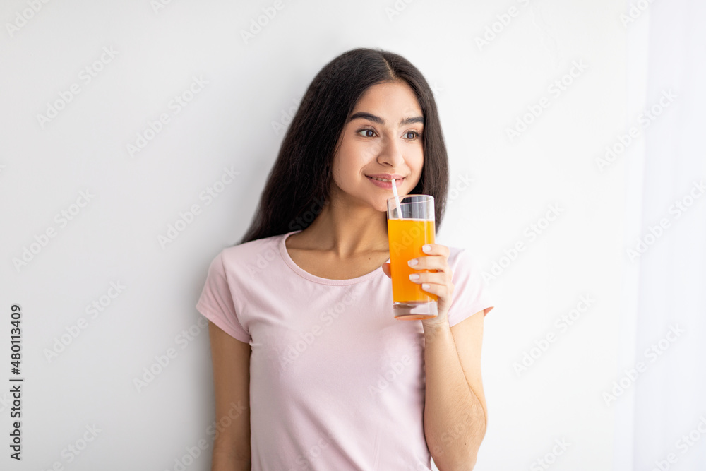 Happy Indian woman holding glass of fruit juice, having refreshing drink at home. Detox, weight loss, dieting concept Happy Indian woman holding glass of fruit juice, having refreshing drink at home. Detox, weight loss, dieting concept