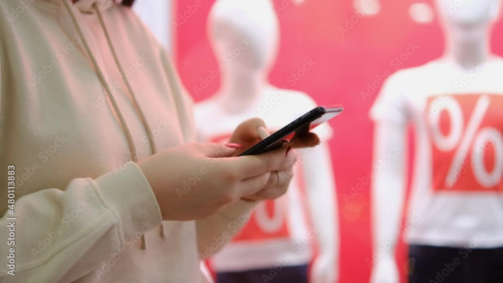Young brunette girl is standing in a department store and texting a message on a smartphone. Woman use mobile phone in shopping mall. Young brunette girl is standing in a department store and texting a message on a smartphone. Woman use mobile phone in shopping mall.