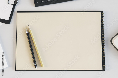 Top view of empty spiral notepad on white desk with keyboard and pencils. Drawing, workplace, supplies and art concept. Mock up, 3D Rendering.