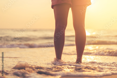 Close up woman legs walking on tropical sunset beach with smooth wave and bokeh sun light wave abstract background. Travel vacation and freedom feel good concept.