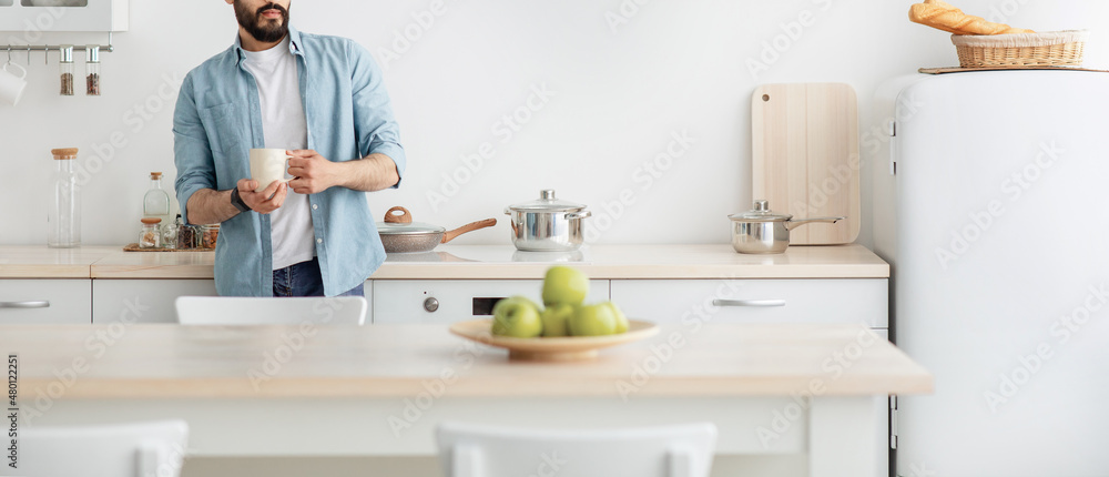 Home relax. Young unrecognizable man drinking morning coffee in kitchen and dreaming, panorama with empty space Home relax. Young unrecognizable man drinking morning coffee in kitchen and dreaming, panorama with empty space