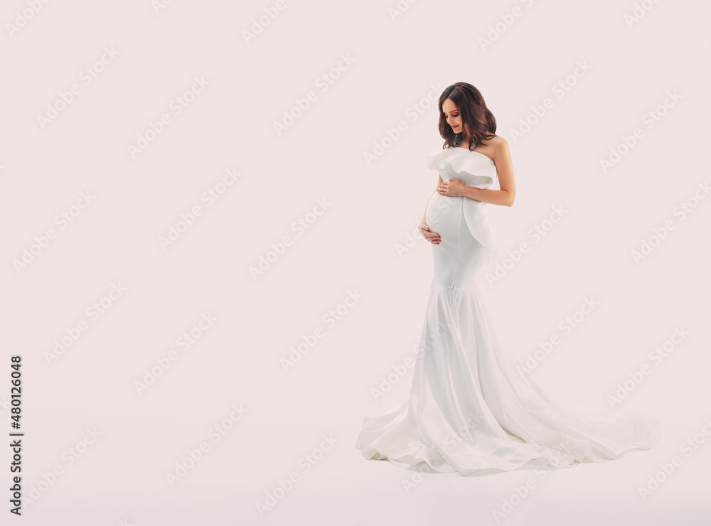 Happy pregnant woman in white dress gently hugs touch her belly with hands. Light beige studio background. Beautiful pregnancy, motherhood, expecting a baby, family health concept. Free space for text Happy pregnant woman in white dress gently hugs touch her belly with hands. Light beige studio background. Beautiful pregnancy, motherhood, expecting a baby, family health concept. Free space for text