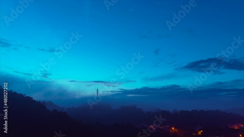 A misty sunrise with partial clouds over a forest hill with 5G Communication tower on top.