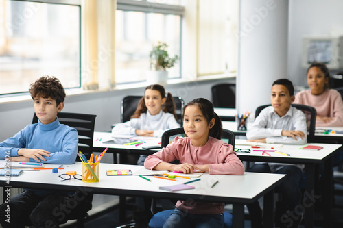 Portrait of focused diverse pupils sitting at desk in classroom