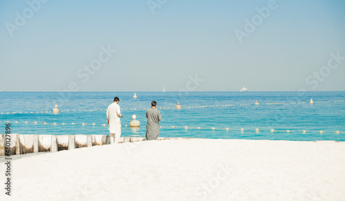 Photography Two men look towards the sea while standing on the sand at Kite Beach in Dubai,