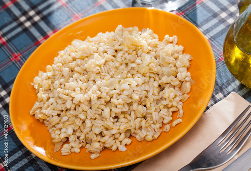 Colorful ceramic plate with cooked pearl barley porridge on checkered textile background photo