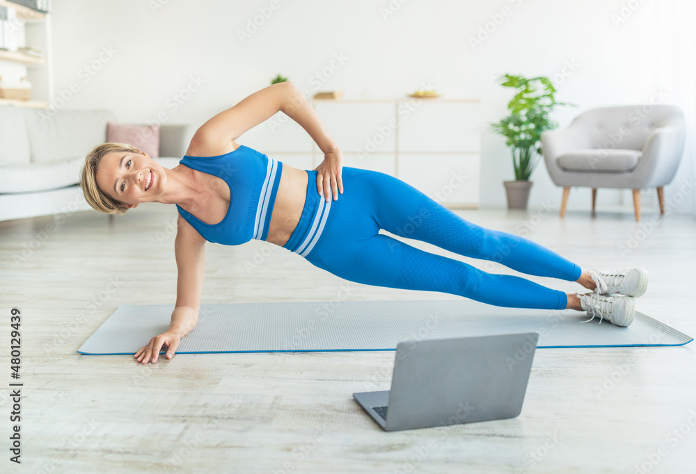 Middle-aged woman doing side plank on mat with pc