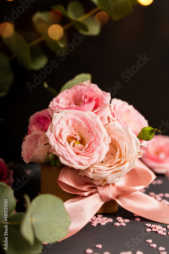 A bouquet of delicate pink roses in a box. Festive vertical card with pink flowers on a dark background  copy space for text