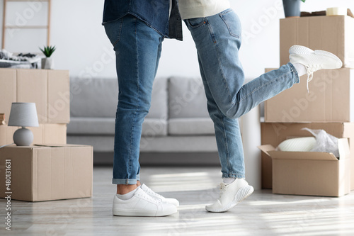 Legs of hugging man and woman standing among moving boxes