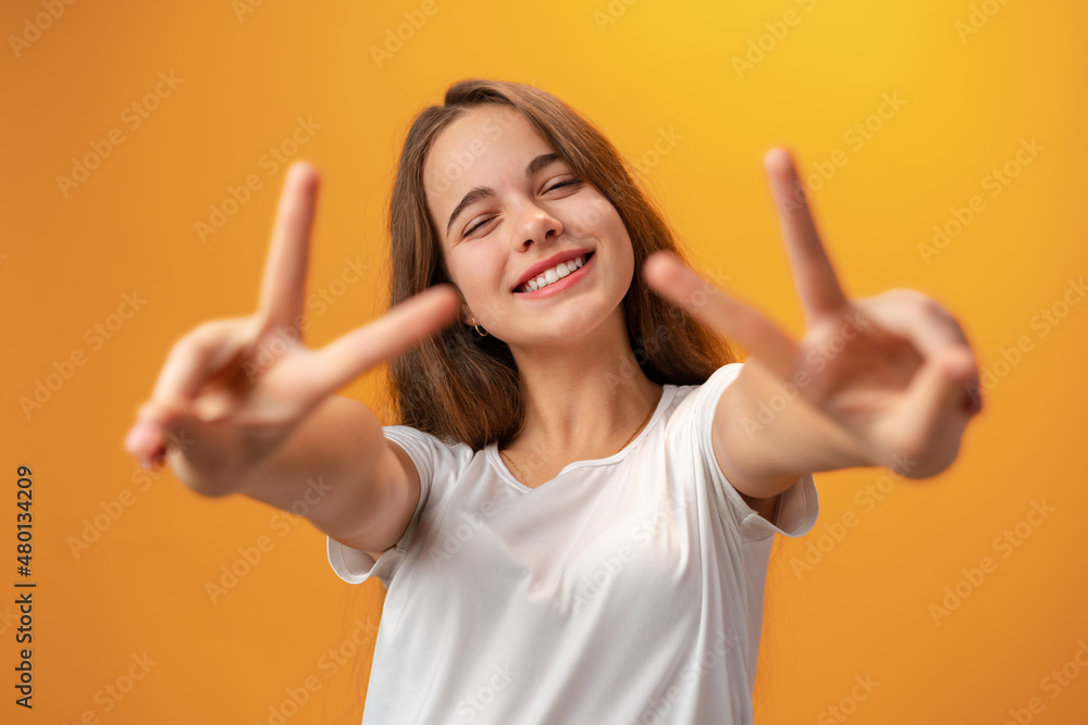 Young caucasian teen girl showing a peace symbol against yellow background Young caucasian teen girl showing a peace symbol against yellow background
