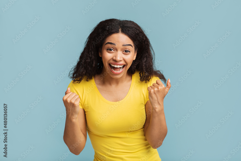 Yes, great news. Portrait of overjoyed black lady screaming and shaking clenched fists over blue studio background Yes, great news. Portrait of overjoyed black lady screaming and shaking clenched fists over blue studio background